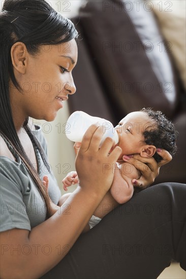 Mixed race mother feeding bottle to newborn baby