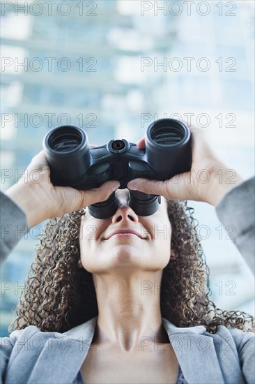 Caucasian businesswoman looking through binoculars