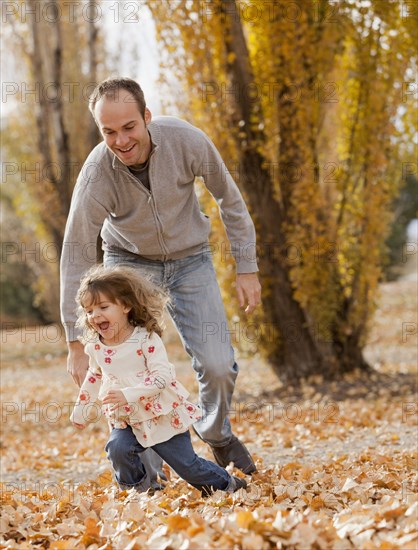 Caucasian father and daughter playing in autumn leaves