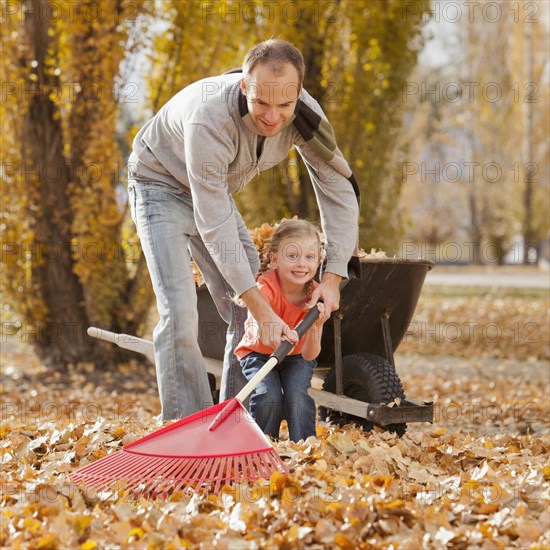 Caucasian father and daughter raking autumn leaves