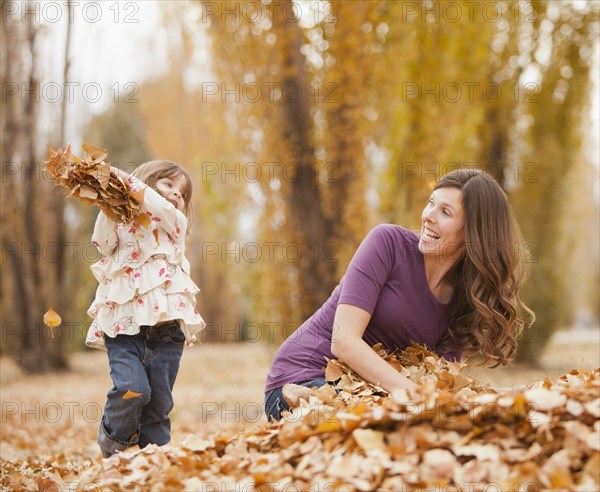 Caucasian girl throwing autumn leaves at mother