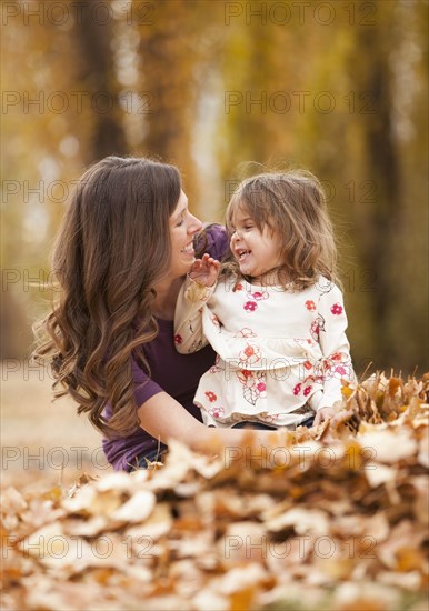 Caucasian mother and daughter playing in autumn leaves