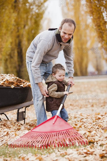 Caucasian father and son raking autumn leaves