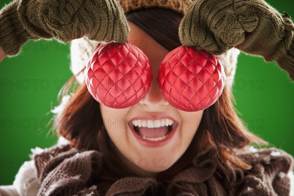 Mixed race woman holding Christmas ornaments in front of her face