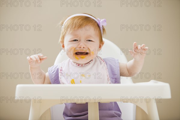 Caucasian baby girl crying in high chair