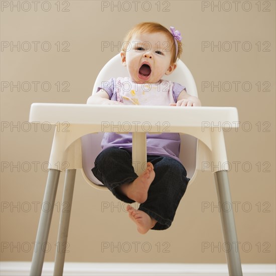 Caucasian baby girl yawning in high chair