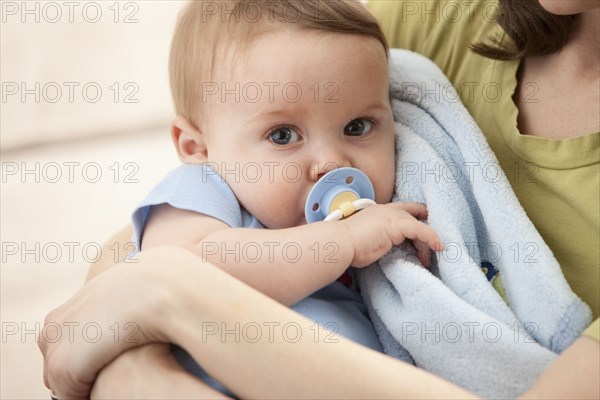 Caucasian baby boy with pacifier in mother's arms