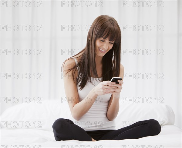 Caucasian woman sitting on bed text messaging on cell phone