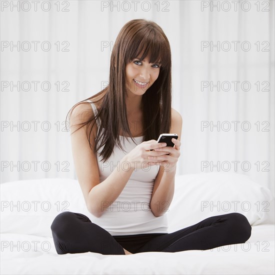 Caucasian woman sitting on bed text messaging on cell phone