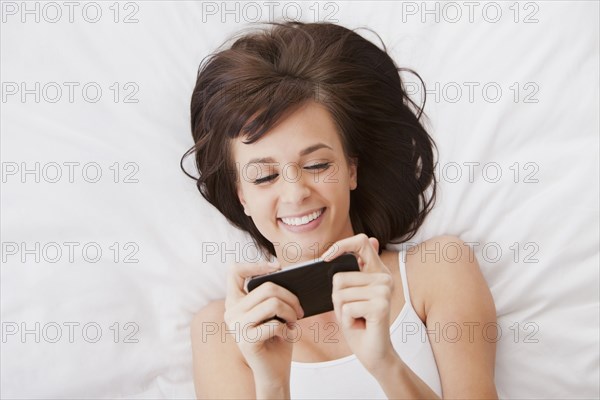Caucasian woman laying in bed text messaging on cell phone