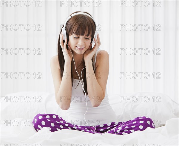 Caucasian woman sitting on bed listening to music on headphones