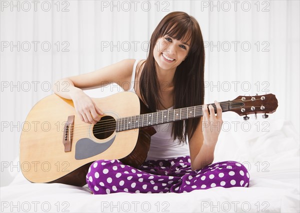 Caucasian woman playing guitar on bed