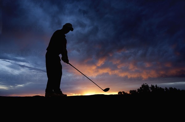 Caucasian golfer swinging golf club at sunset