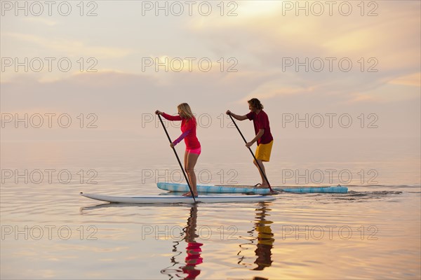 Caucasian couple standing on paddle boards