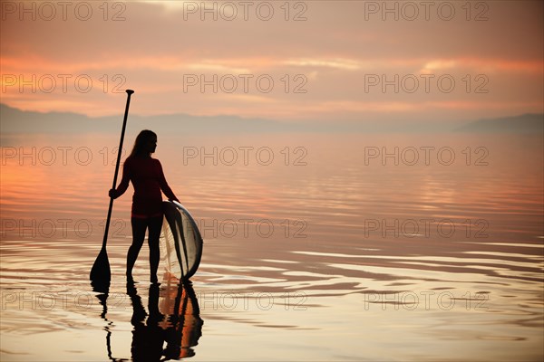 Caucasian woman standing with paddle board at sunset