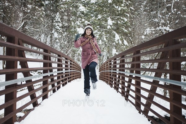 Caucasian woman crossing snow covered bridge