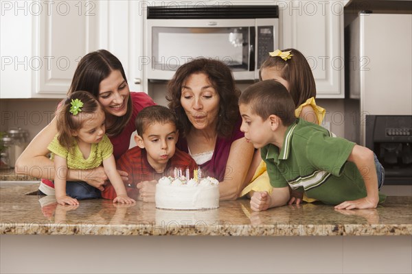 Caucasian family in kitchen blowing out birthday cake