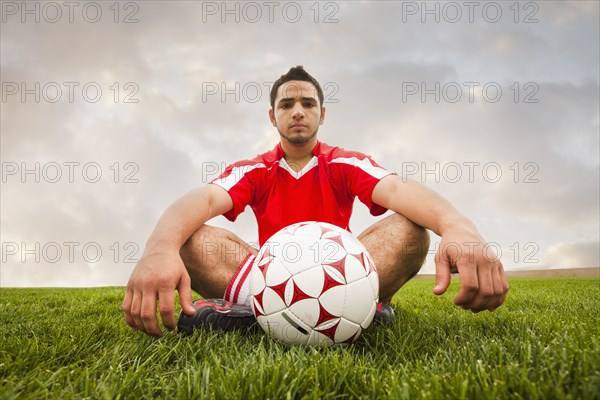 Hispanic soccer player sitting with ball