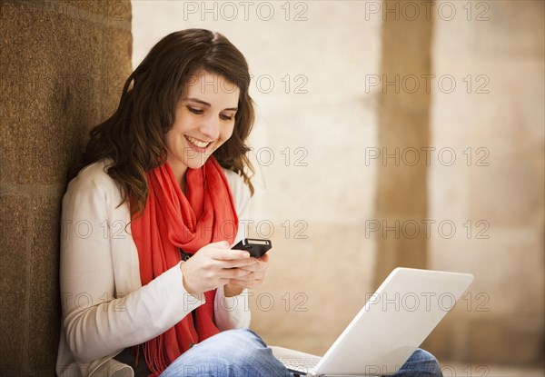 Caucasian woman sitting with laptop and text messaging on  cell phone