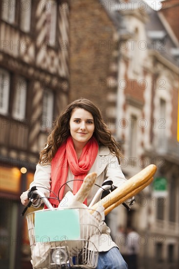 Caucasian woman riding bicycle with bread in basket