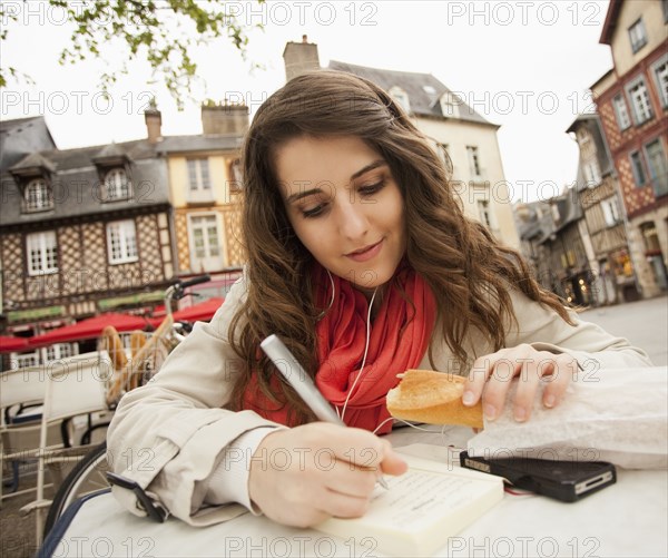 Caucasian woman eating bread and writing in book