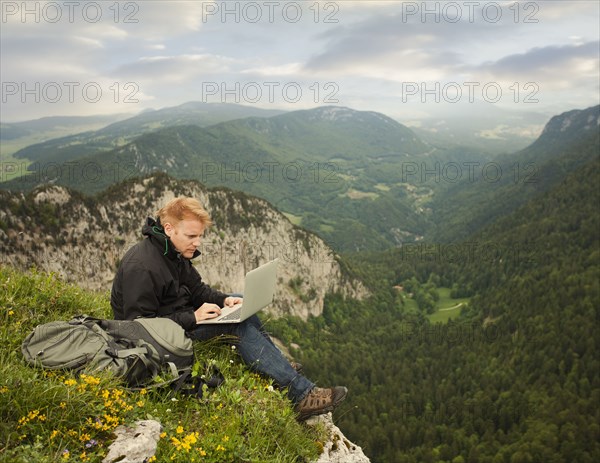 Caucasian man using laptop on remote cliff's edge