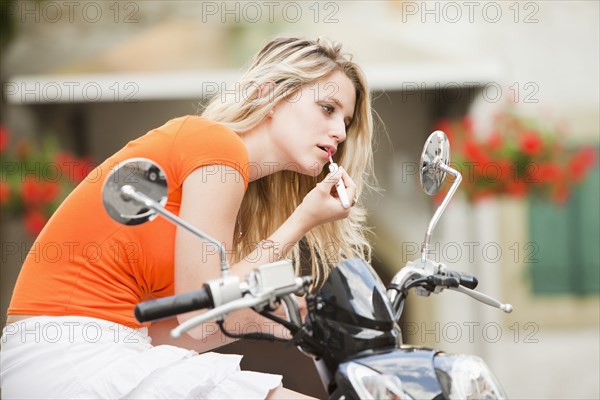 Caucasian teenager sitting on scooter putting on lipstick