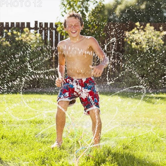 Caucasian boy playing in sprinkler