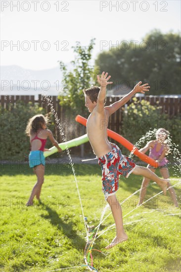 Caucasian children playing in the sprinkler