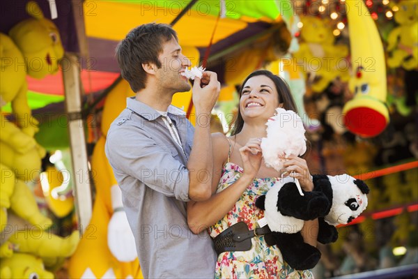 Caucasian couple sharing cotton candy at carnival