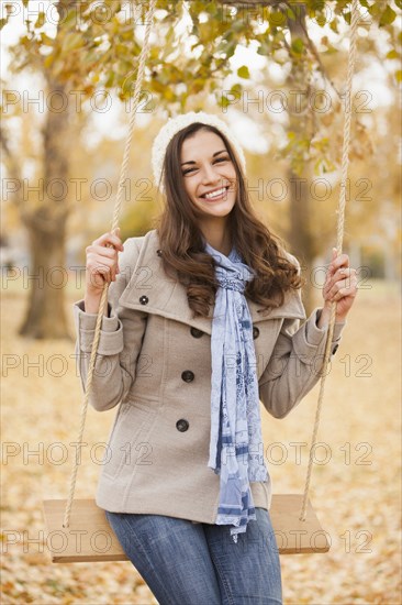 Caucasian woman sitting on swing in autumn leaves