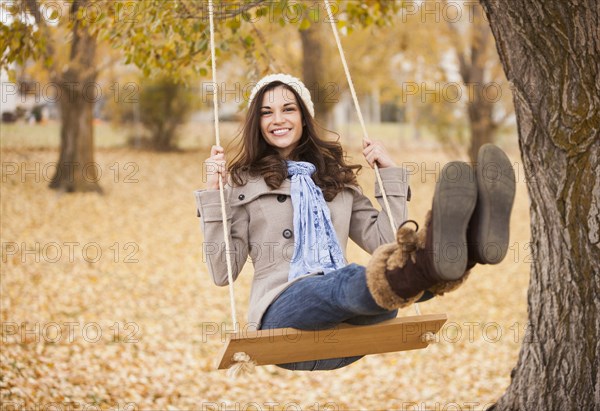 Caucasian woman sitting on swing in autumn leaves