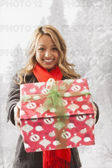 Mixed race woman offering present in snow