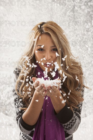 Mixed race woman blowing handful of snow