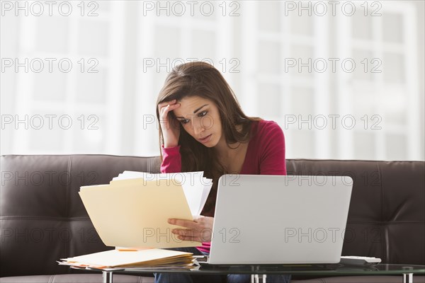 Caucasian woman reading papers at laptop