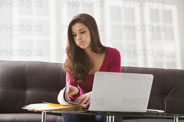 Caucasian woman reading papers at laptop
