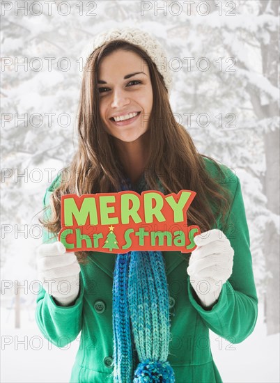 Caucasian woman holding 'Merry Christmas' sign in snow