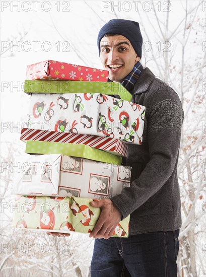 Hispanic man holding Christmas gifts in snow