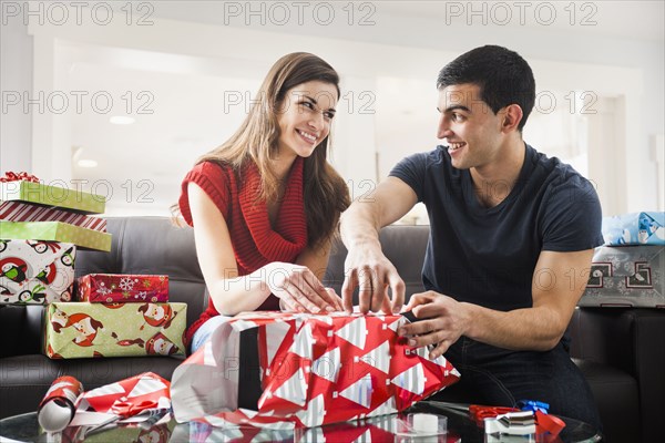 Couple wrapping Christmas presents in living room