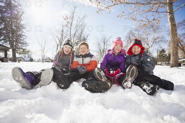 Caucasian children sitting in snow outdoors