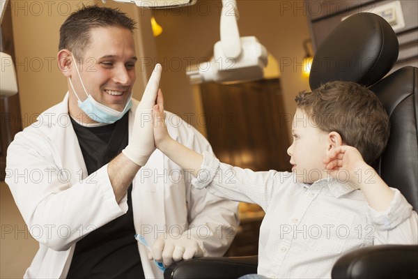 Caucasian dentist and boy high fiving in office