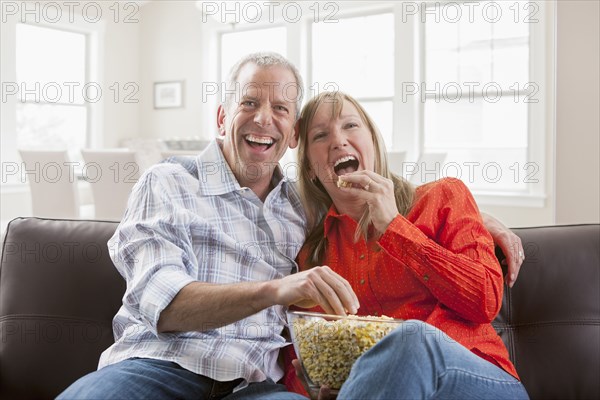 Caucasian couple eating popcorn on sofa