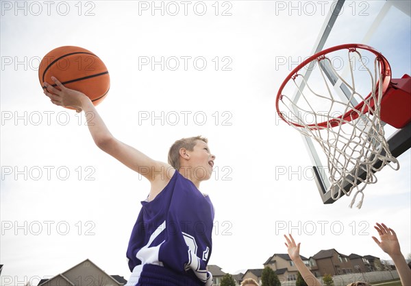 Caucasian boy dunking basketball in hoop