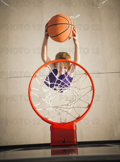 Caucasian boy dunking basketball in hoop