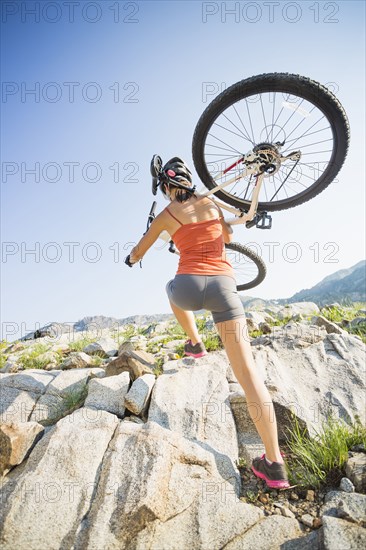 Caucasian woman carrying mountain bike on rocky hillside