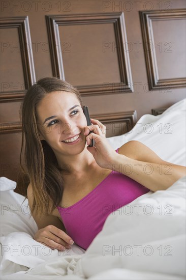 Caucasian woman talking on cell phone in bed