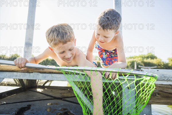 Caucasian boys using fishing net on dock