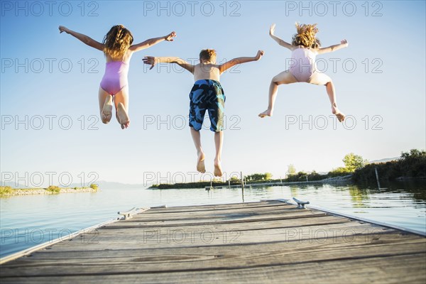 Caucasian children jumping off dock into lake