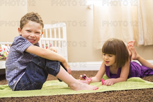 Caucasian girl painting brother's toes