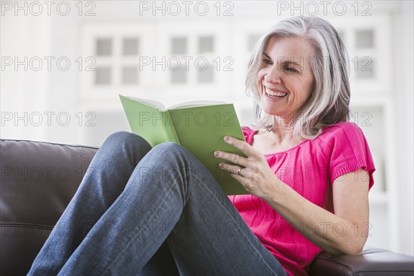 Happy Caucasian woman reading book on sofa